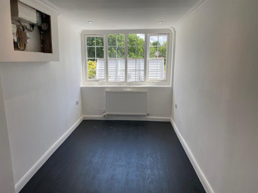 A sparsely furnished room with a window, white walls, and a dark floor.
