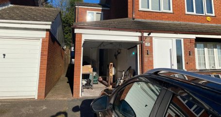 Garage conversion in Birmingham A garage entrance with tools and items inside, alongside a parked car.