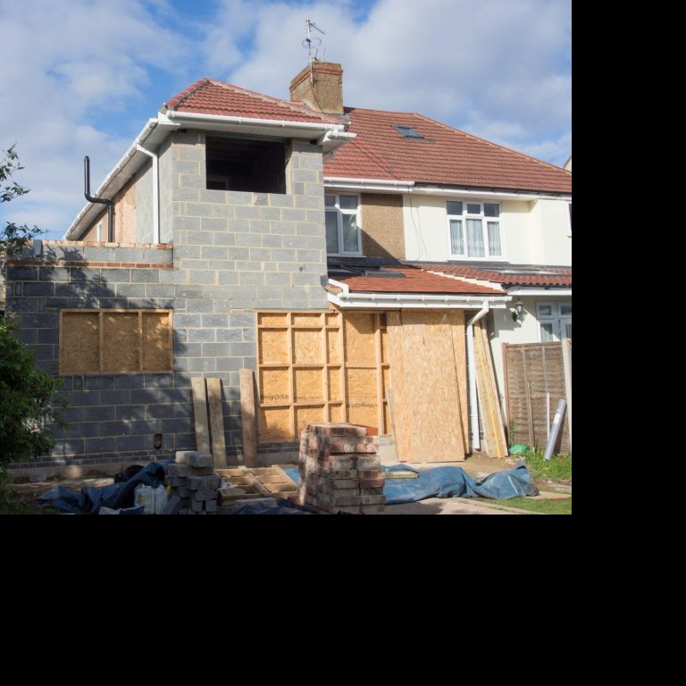Construction of a house extension with grey blockwork and boarded windows.