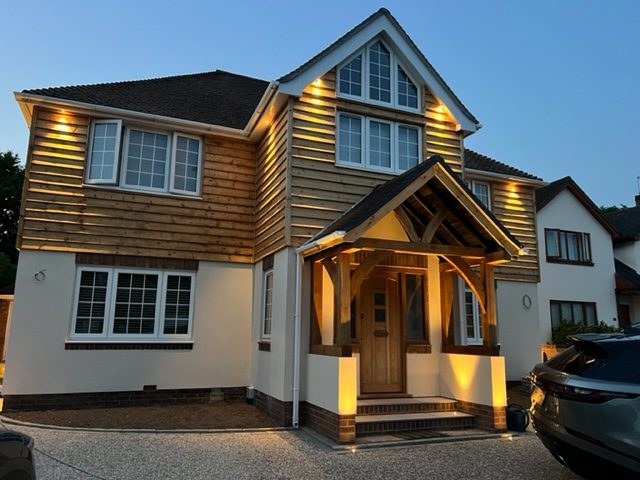 Front Porch Extension A modern two-toned house with wooden cladding and an illuminated entrance.