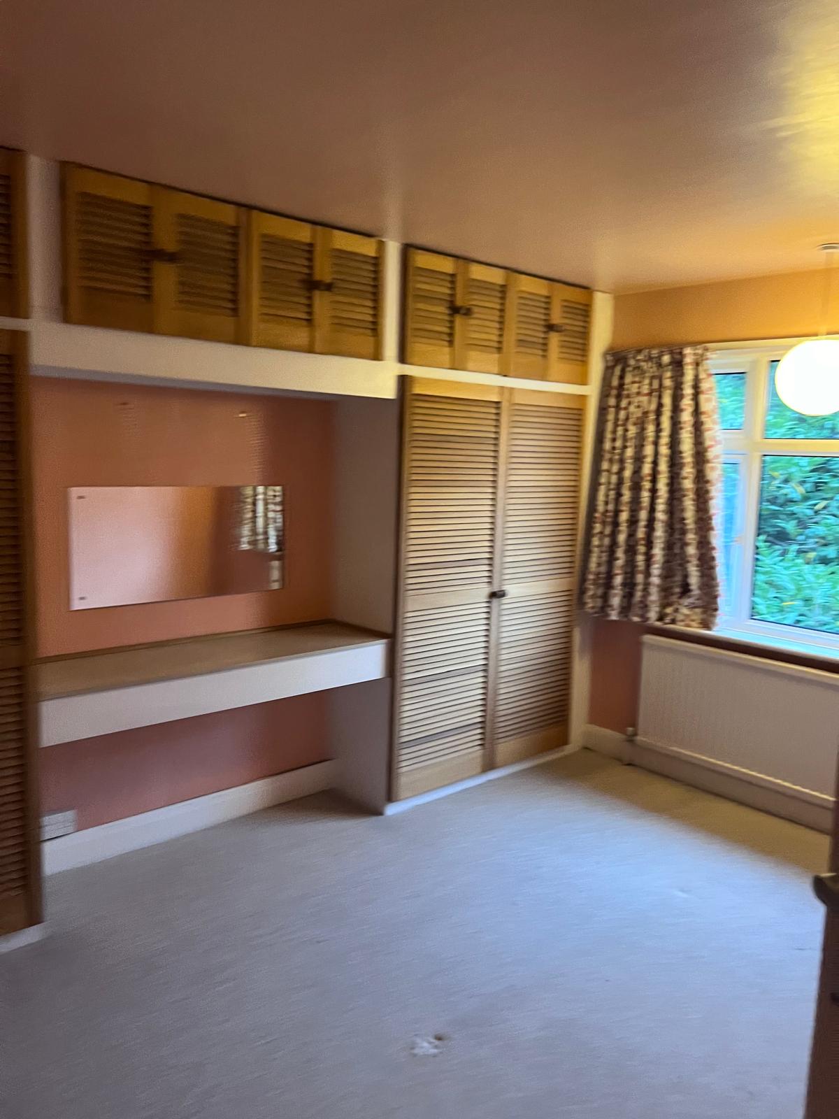 Existing Empty bedroom with light pink walls, a built-in wardrobe, and a window with curtains.