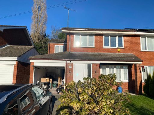 A brick semi-detached house with a garage and sunlight reflecting on the window.