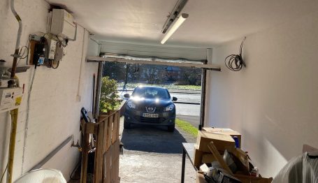 Garage conversion in Birmingham A garage interior with a car visible outside and wooden storage in the foreground.