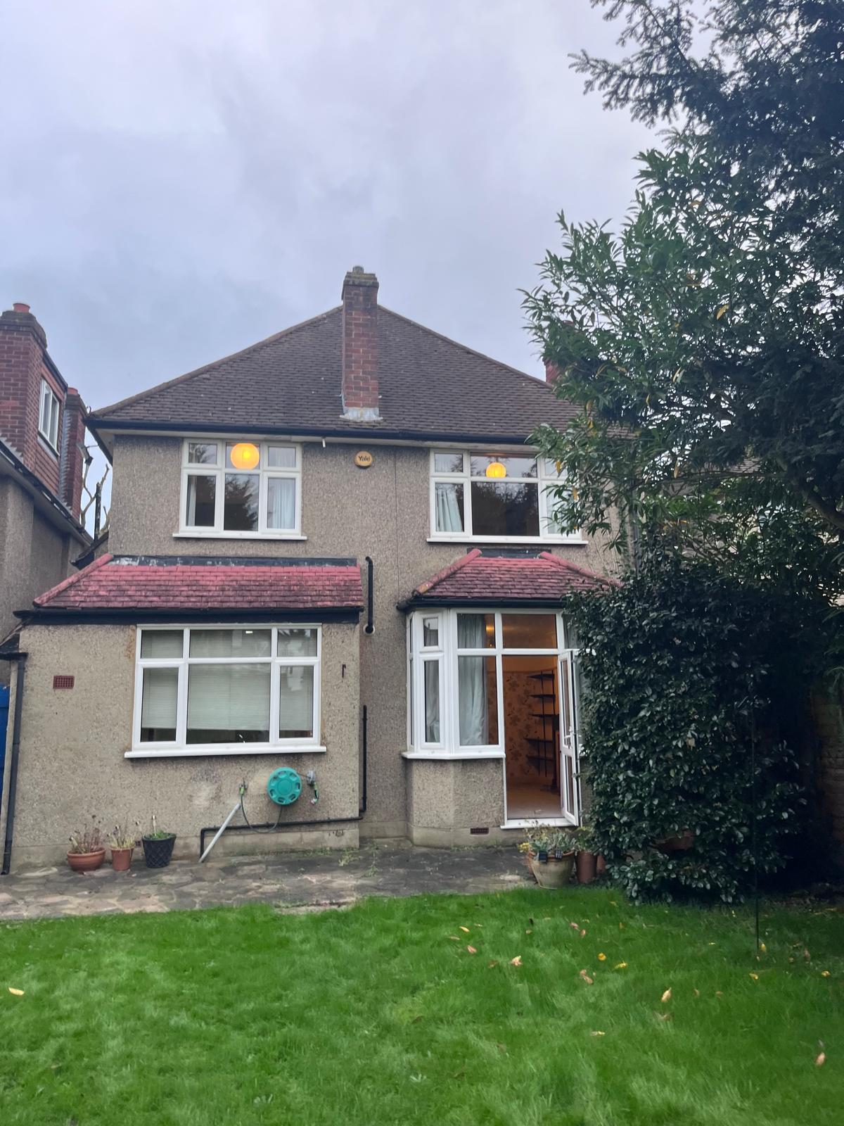 Existing Two-storey house with a front garden and large windows, surrounded by greenery.