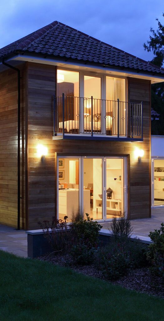 Double-Storey Rear Extension Modern two-storey house with wooden facade, lit windows, and evening sky.
