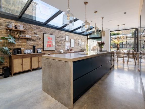 Wraparound Extension Modern kitchen with a concrete island, wooden furniture, and large glass windows.