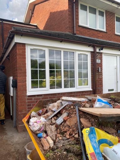 Pile of rubble and debris in front of a house with a large window.